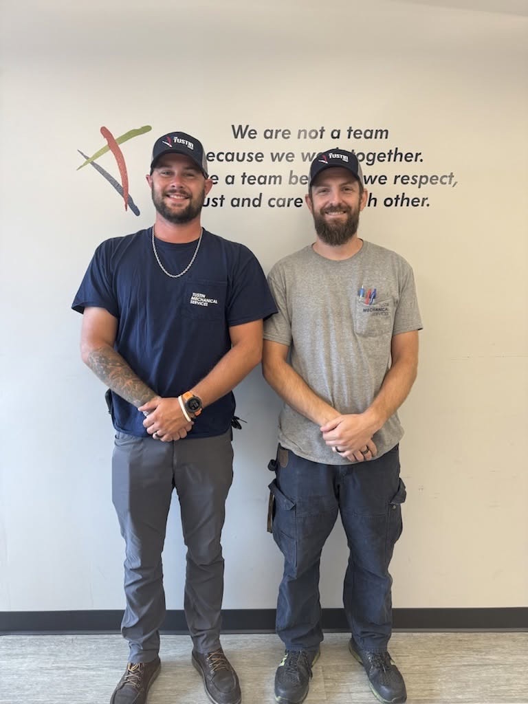 Two Tustin team members standing beneath the company teamwork message