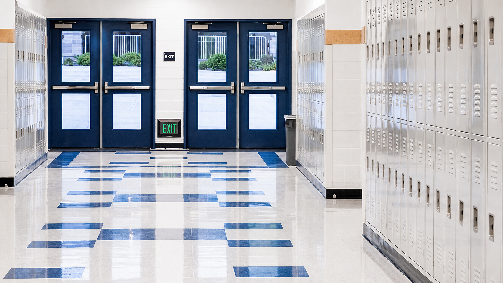 Clean high school hallway with lockers, polished floors and exterior exit doors in a modern educational facility.